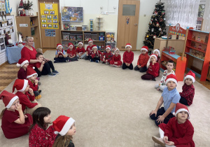 Dzieci siedzą w kole w czapkach mikołajokowych.