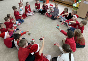 Dzieci siedzą w kole na dywanie i trzymają zrobione bombki.
