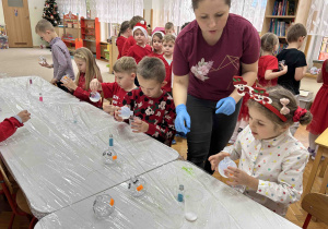 Dzieci przy stoliczkach ozdabiają bombki.