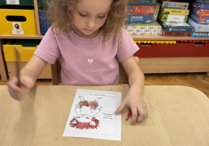 Dziewczynka koloruje ilustrację z postacią Gniewka.