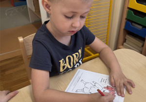 Chłopiec trzyma w ręku czerwoną kredkę i koloruje włosy Gniewka.