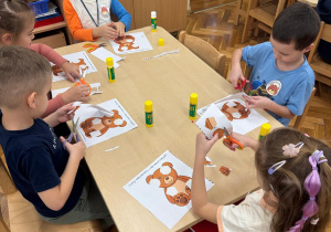 Dzieci przyklejaj do misia odpowiednie części.