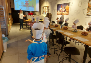 Dzieci stoją ibiorą udział w zabawie, pokazują jak kręcą ciasto na pierniczki.