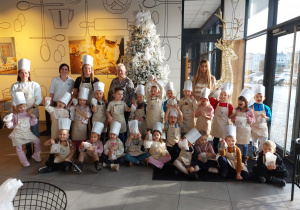 Dzieci z paniami pozują do wspólnego zdjęcia przy choince w piekarni.