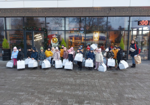 Dzieci stoją przed piekarnią z prezentami w ręku.