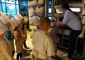 Dzieci stoją przy piecu do wypieku bułek.