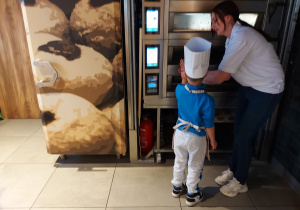 Chłopiec przy pomocy pani sprawdza temperaturę pieca do wypieku bułek.