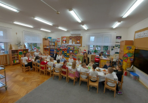 Dzieci z paniami siedzą przy stole przed rozpoczęciem jedzenia potraw wigilijnych.