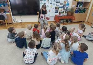 Dzieci siedzą na dywanie i uważnie słuchają tekstu.