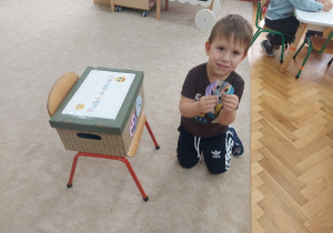 Chłopiec będzie przyklejał do pudełka wesołą emotkę.