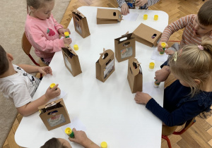 Dzieci samodzielnie przyklejają życzenia na pudełko.