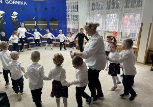 Dzieci i panie tańczą w kole trzymając się za ręce.