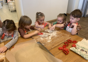 Dzieci posypują ciasto mąką, żeby się nie przykleiło do stolnicy.