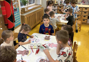 Dzieci pracują przy stoliczkach malując pierniczki.