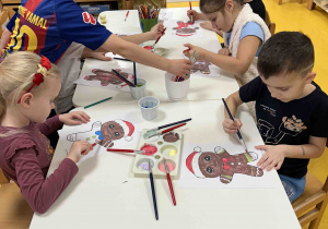Dzieci pracują przy stoliczkach malując pierniczki.