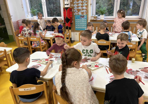 Dzieci pracują przy stoliczkach malując pierniczki.
