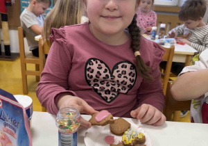 Uśmiechnięta dziewczynka pokazuje jak ozdabia pierniczki.