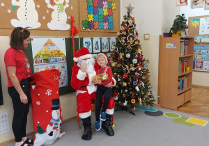 Chłopiec siedzi z prezentem u mikołaja na kolanach