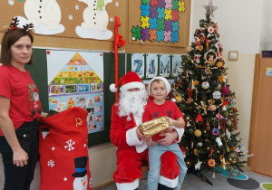 Chłopiec siedzi z prezentem u mikołaja na kolanach