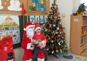 Chłopiec siedzi z prezentem u mikołaja na kolanach