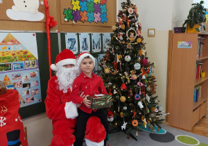 Chłopiec siedzi z prezentem u mikołaja na kolanach