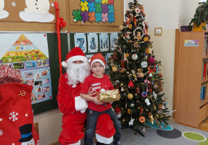 Chłopiec siedzi z prezentem u mikołaja na kolanach