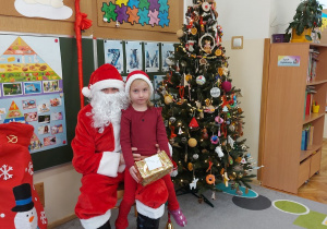 Dziewczynka siedzi z prezentem u mikołaja na kolanach