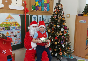 Chłopiec siedzi z prezentem u mikołaja na kolanach