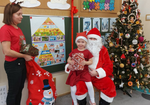 Dziewczynka siedzi z prezentem u mikołaja na kolanach