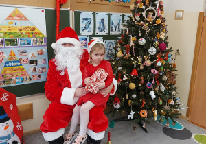 Dziewczynka siedzi z prezentem u mikołaja na kolanach