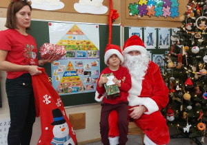 Chłopiec siedzi z prezentem u mikołaja na kolanach