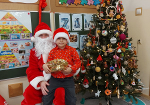 Chłopiec siedzi z prezentem u mikołaja na kolanach