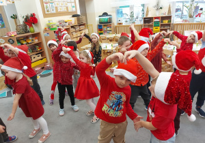 Dzieci ubrane w mikołajkowe czapeczki i czerwone stroje tańczą dla mikołaja