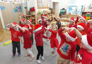 Dzieci ubrane w mikołajkowe czapeczki i czerwone stroje tańczą dla mikołaja