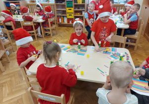 Dzieci siedzą przy stolikach i skejają kolorowe łańcuchy