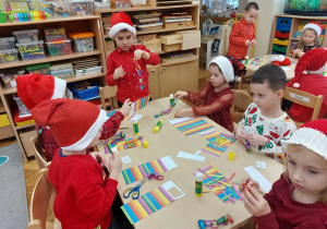 Dzieci siedzą przy stolikach i skejają kolorowe łańcuchy