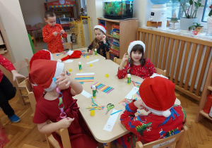 Dzieci siedzą przy stolikach i skejają kolorowe łańcuchy