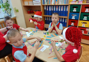 Dzieci siedzą przy stolikach i skejają kolorowe łańcuchy