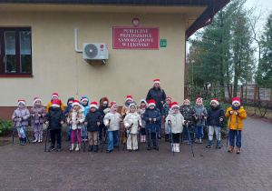 Dzieci z panią stoją z kijkami na tle budynku przedszkola