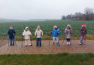 Dzieci stoją na chodniku trzymając w dłoniach kijki