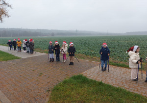 Dzieci stoją na chodniku trzymając w dłoniach kijki