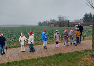 Dzieci stoją na chodniku trzymając w dłoniach kijki