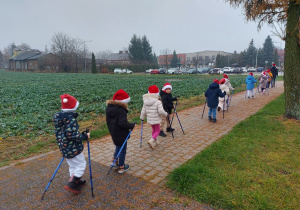 Dzieci w mikołajkowych czapkach idą z kijkami