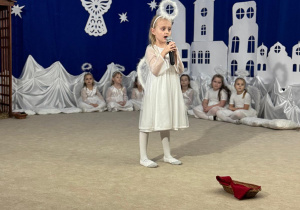 Dziewczynka śpiewa pastorałkę do mikrofonu.