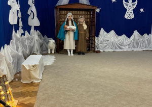 Maryja i Józef stoją w szopce z dzieciątkiem na rękach.