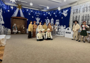 Pasterze, gospodarze i owieczki śpiewają i grają na instrumentach.