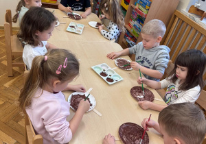 Dzieci malują papierowe talerzyki farbami.