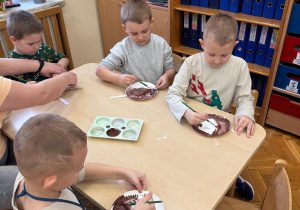 Chłopcy malują farbami papierowe talerzyki.