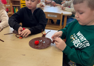 Chłopcy przyklejają rogi reniferom.