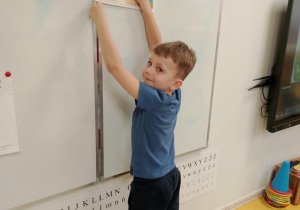 Chłopiec przyczepia do tablicy rysunek.